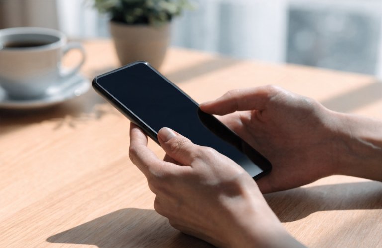 Des mains tenant un téléphone portable posé sur la table, l'écran étant dépourvu d'applications ouvertes.