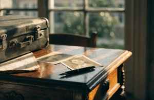 Mala antiga, mapa dobrado e retratos sépia sobre escrivaninha de madeira