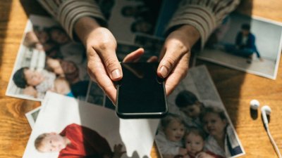 Celular sobre a mesa cercado de fotos impressas e fones de ouvido