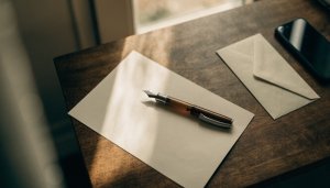 Folha de papel em branco com caneta tinteiro e envelope sobre uma mesa de madeira